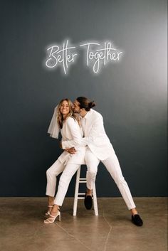 two people sitting on a stool in front of a wall with the words better together