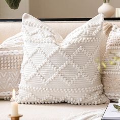 a close up of a pillow on a couch with a book and candles in the background