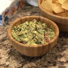 two wooden bowls filled with guacamole and tortilla chips on a counter