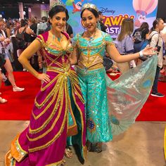 two women dressed in colorful costumes posing for the camera at an amusement park or convention