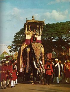 an elephant is dressed in red and gold with people standing around it while others look on