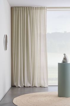 a round rug in front of a window with curtains and a vase on the floor