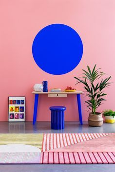 a living room with pink walls and blue circles painted on the wall above it is a small table, stools, and potted plants