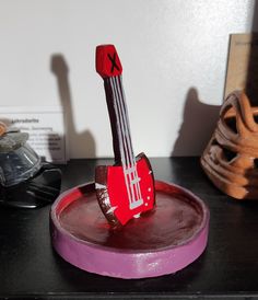 a red and white toy guitar sitting on top of a purple plate