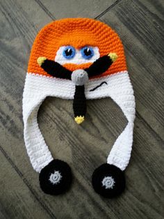 an orange and white knitted hat sitting on top of a wooden floor next to a pair of blue eyes