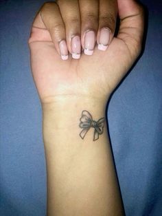 a woman's arm with a bow tattoo on it, and her left hand holding the wrist