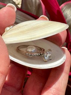 a person holding an open shell with a ring in it's middle and a diamond on the inside