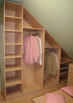 an attic bedroom with closets and clothes hanging on the shelves, along with a bed