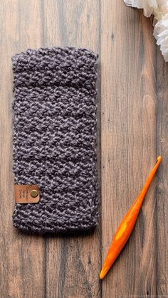 a crocheted cell phone case sitting on top of a wooden table next to flowers