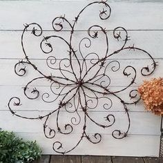 a metal wall hanging on the side of a white building with a plant next to it