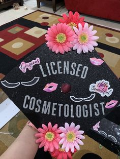 a decorated graduation cap with pink flowers on the front and black lettering that reads, license cosmetologists