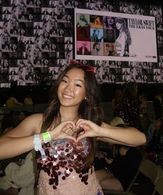 a woman making a heart with her hands in front of a wall full of pictures