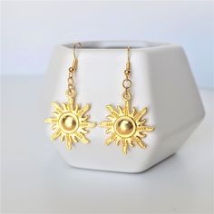 A pair of radiant gold sun earrings featuring bright gold tone dangle charms and earwires. Gold charms are plated alloy. Each set comes with a pair of rubber backs and ear wires are hypoallergenic and nickel free. Please be advised - if your ears are extremely sensitive, they are NOT sterling silver. Jewelry Care Tips For a Long, Happy Life Together <3 * Store your jewelry in an air-tight container to avoid metal parts becoming tarnished or oxidized * Remove Jewelry before exercise or swimming * Gold Sun-shaped Earrings For Gift, Gold Sunburst Earrings With Sun Design, Nickel Free Gold Earrings For Summer, Gold Sunburst Earrings For Gift, Gold Brass Earrings With Sun Design, Gold Drop Earrings With Sun Design, Gold Jewelry With Sun Design Drop Earrings, Gold Celestial Earrings With Sun Design, Gold Dangle Earrings With Sun And Moon Design