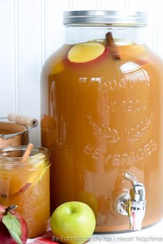 two jars filled with apple cider next to apples