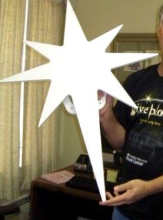 a man standing in front of a computer desk holding up a paper cut out of a star