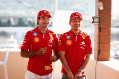 two men standing next to each other wearing red shirts and white pants with yellow letters on them