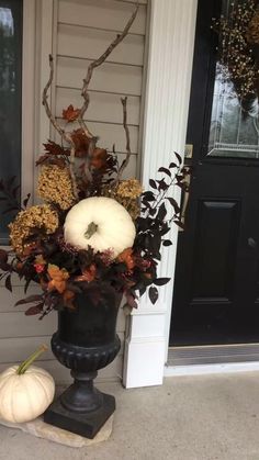 a black vase with white pumpkins and flowers on the front porch next to a door