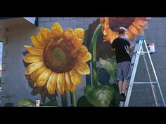 a man is painting a sunflower on the side of a building with a ladder