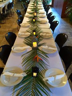 a long table is set with white plates and palm leaves