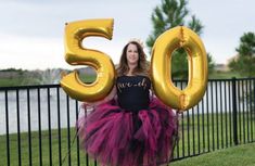 a woman standing in front of a fence holding up the numbers 50 and fifty balloons