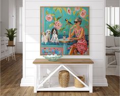 a woman sitting at a table with two dogs in front of her and a painting on the wall behind her