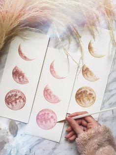 a person is painting phases of the moon on paper with watercolors and brush