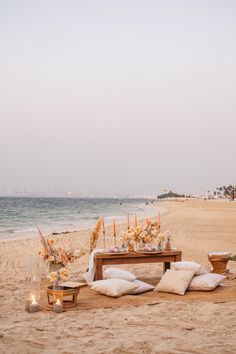 a table set up on the beach with candles and flowers