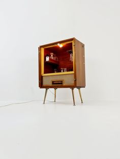 a small wooden cabinet with shelves and lights on it's sides, in front of a white wall