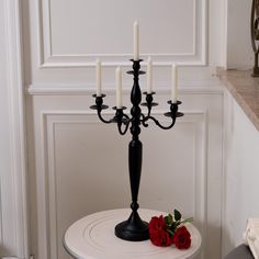 a black candelabra with four candles on it and two roses sitting on the table