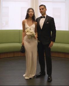 a man and woman standing next to each other in front of a green couches