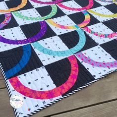 a black and white checkerboard quilt with colorful circles on the center, sitting on top of a wooden table