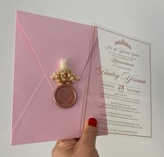 a person holding up a pink envelope with a wax stamp on it and a wedding ring