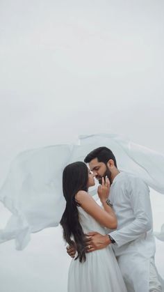 a man and woman standing next to each other in front of a white cloth draped over them