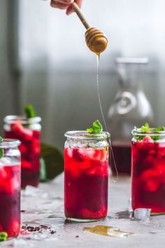 a person is spooning honey into jars filled with red liquid