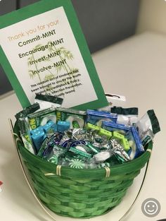 a green basket filled with assorted items sitting on top of a table next to a sign