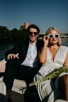 a man and woman sitting next to each other on a boat in the water wearing sunglasses