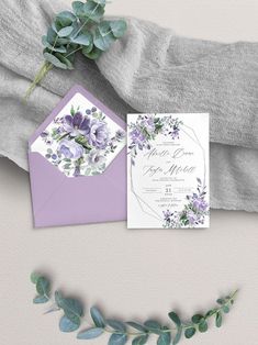 the wedding stationery is laid out on top of an envelope with purple flowers and greenery