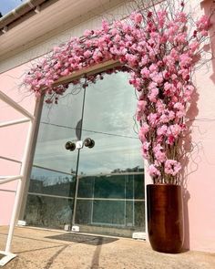 a tall vase with pink flowers sitting in front of a window on the side of a building