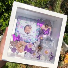 a person holding up a white box with purple flowers and butterfly decorations in front of it