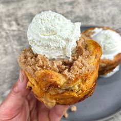 a hand holding an ice cream filled pastry on top of a gray plate next to another piece of bread