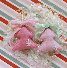 two pink and one green christmas tree ornaments sitting on top of some glittery material