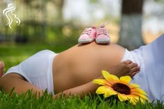 a pregnant woman laying in the grass with a sunflower on her belly and wearing pink tennis shoes