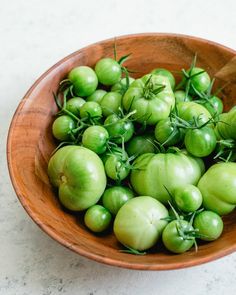 a wooden bowl filled with green tomatoes on top of a white countertop next to a wooden spoon