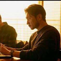 two men sitting at a table working on their laptops in front of the window