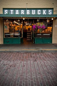 a store front with flowers in the window and brick sidewalk on one side that leads up to it