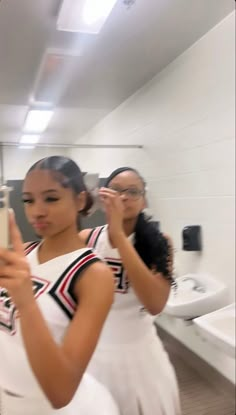 two young women taking pictures in a bathroom mirror