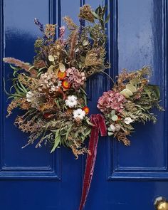 a blue door with a red ribbon and some flowers on it's front side