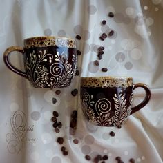 two coffee mugs sitting next to each other on top of a white table cloth