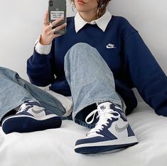 a woman sitting on top of a bed holding a cell phone in one hand and a pair of blue sneakers in the other