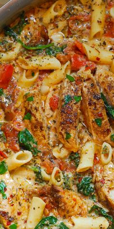 a casserole dish with pasta, spinach and tomatoes in a white sauce